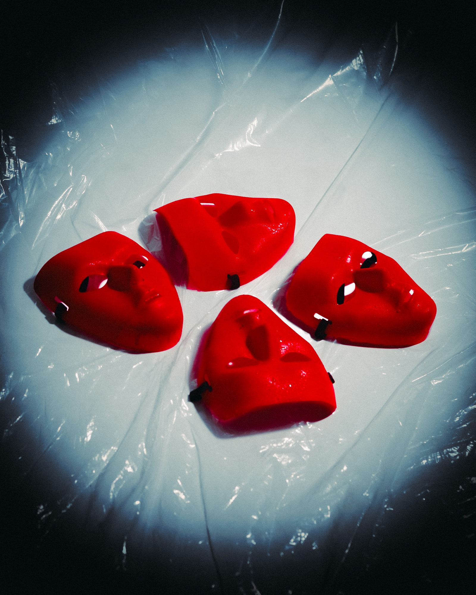 Four glossy red face masks lying on a sheet of plastic in a pool of light.