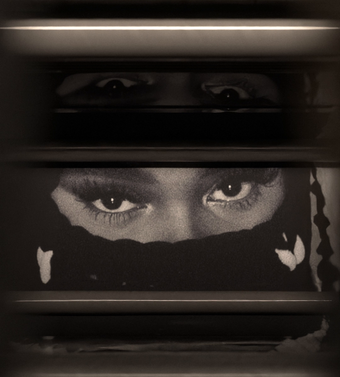 Eyes in a black and white portrait look up from under running water, between the steel rollers of a wash tank.