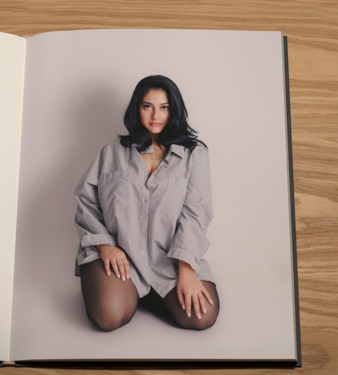 A person in an oversized grey shirt kneels and looks straight at the camera.