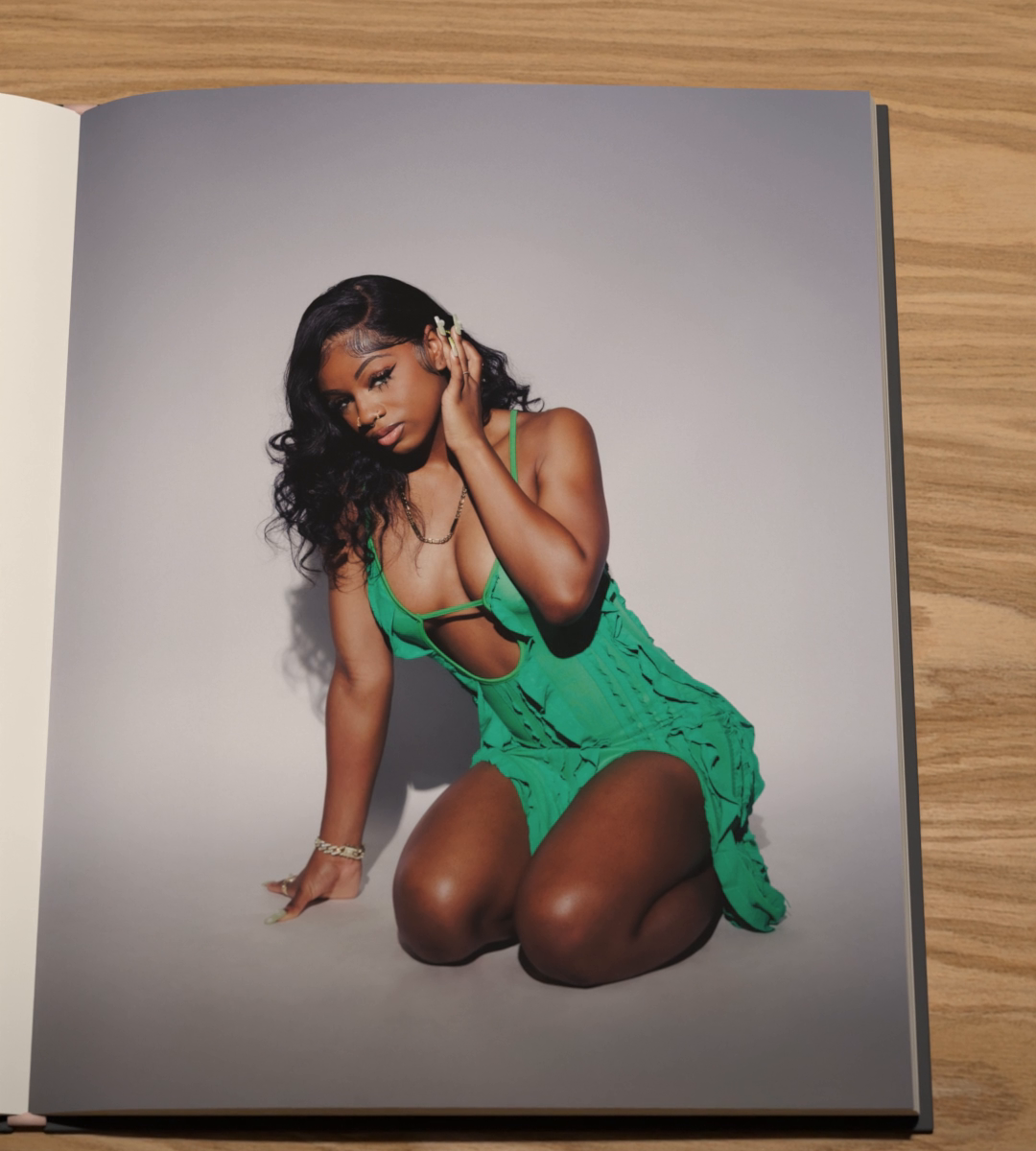 A person in a green knitted dress kneels, one hand in their hair.