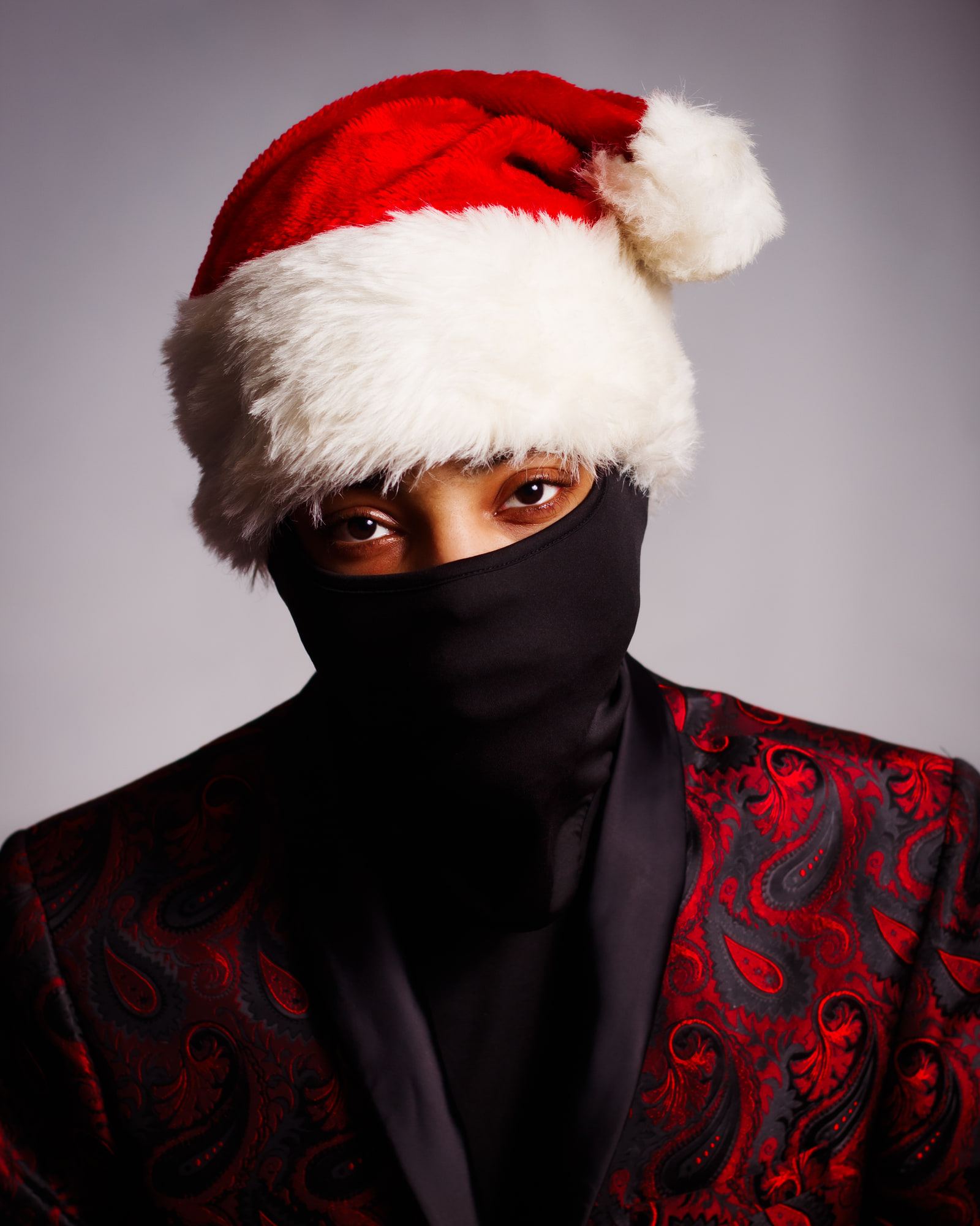 Self-portrait in a red and white Santa hat, a black face covering and a red paisley jacket.