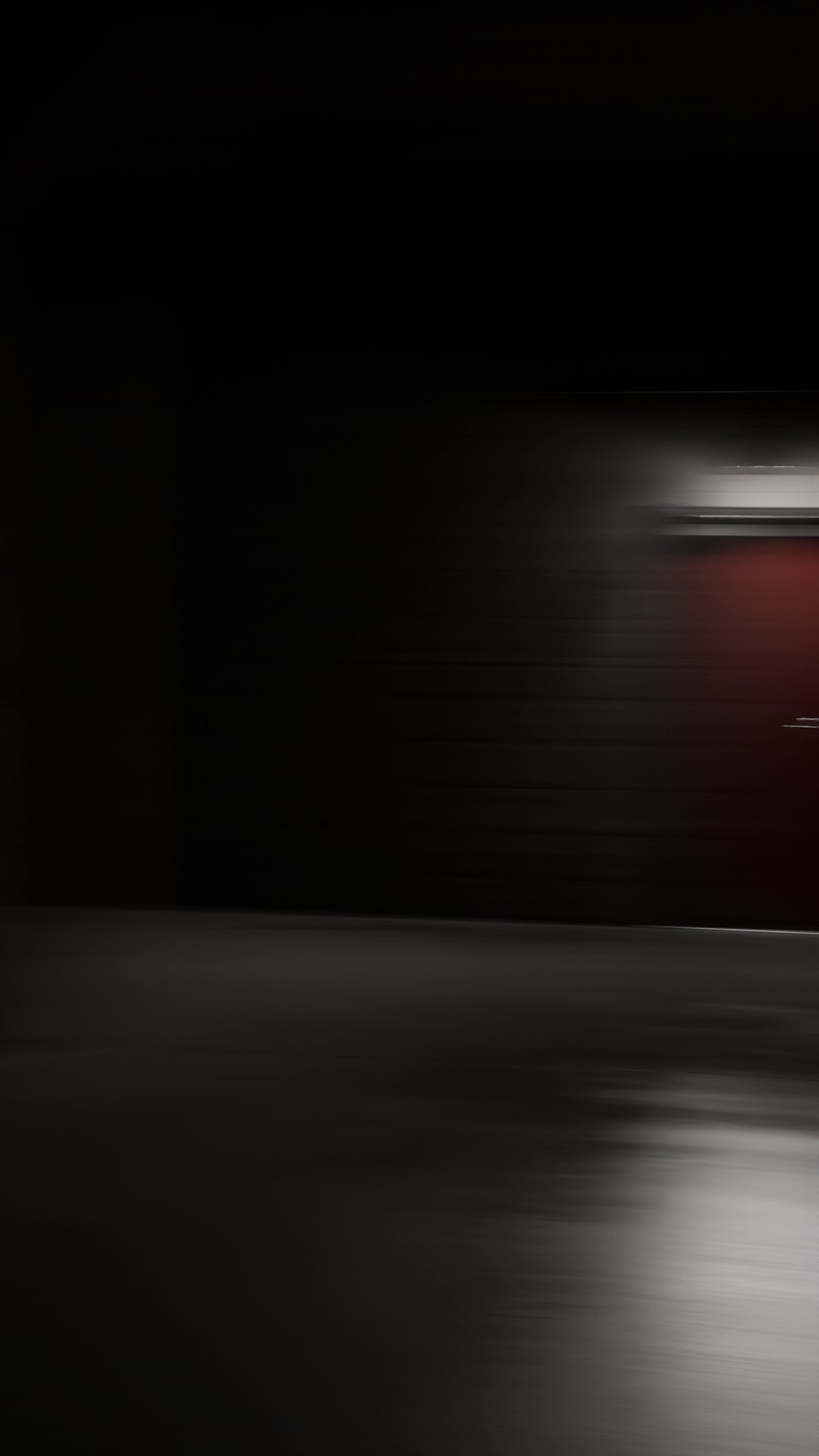 Mid-turn and blurred by the movement, the lit red door slides out past the right edge of the frame. The rest is dark hall, with a pale smear of lamplight on the floor.